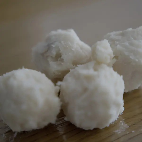 Gros plan sur des morceaux de beurre de karité brut à la surface irrégulière, teinte ivoire.